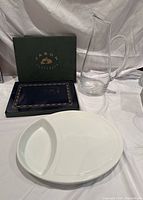 Six navy blue lunch placemats in box, rectangular navy blue and gold cheese plate, and tall clear glass wine or water decanter with handle