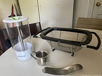 Tall transparent herb crisper container with white lid, sink strainer, small creamer and garlic mincer on table