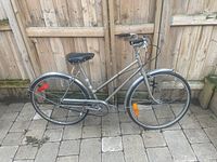 Full side view of gray ladies bicycle showing step-through frame, black saddle, fenders, and tires with reflectors