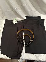 Two pairs of ladies dress pants (dark colors) and one brown leather belt placed on fabric background.