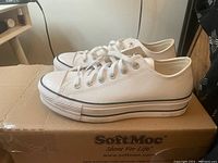 Side and top view of the ladies Converse white leather sneaker on cardboard box.