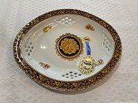 Top view of Limoges oval porcelain plate showing Bacchus face design and intricate gold and black border with lattice cutouts.