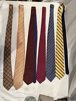 Seven men's silk designer ties laid out flat showing full length and patterns.