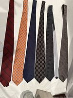 Seven men's silk ties laid out displaying a variety of patterns and colors.