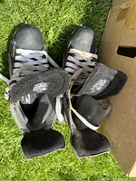 Top view photo of one pair of men’s black and white ice skates size 8.5 EEE, tongues lifted, on grass.