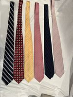 Six men’s silk ties laid side by side showing different colors and patterns including stripes, squares, and checks.