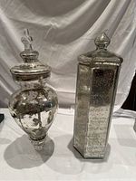 Two mercury glass ginger jars with distinctive shapes and lids, photographed against white backdrop.
