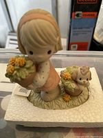 Porcelain figurine of a blonde girl in pink dress holding flower pots with a small dog on grassy base.