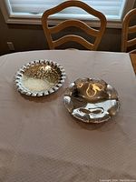 Two silver plated serving dishes on dining table with scalloped and ornate edges.