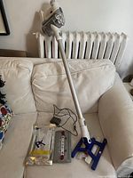 Dyson DC57 cordless stick vacuum cleaner with charger and cleaning wipes displayed on white couch.