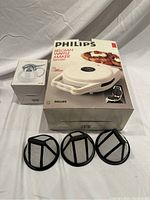 Full view of Philips waffle maker box, glass honey jar, and the three black plastic coffee filters placed in front.