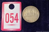 Photo showing the 1972 Canadian silver dollar next to a red and white lot number card for size reference.