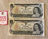 Top view of two 1973 Canadian one dollar notes with sequential serial numbers.