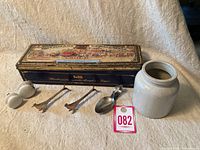 Overview of the antique lot showing all items including tin box, ceramic jar, utensils, spoon, and eyeglasses.