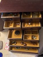 Top view of opened jewelry case showing multiple compartments with various earrings, rings, pins, and bracelets arranged neatly