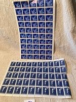 Two sheets of Canadian mint postage stamps featuring blue and white John G. Diefenbaker 17 cent profile stamps laid on beige fabric.