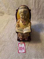 Front view of ceramic grandma figurine seated in a rocking chair holding 'RETIREMENT FUND' book.