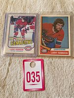 Two Larry Robinson hockey cards displayed side by side on fabric surface, including one card in protective plastic with 'Canadiens' and 'Defense' text visible.