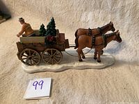 Side view showing the two horses harnessed to the wagon, the male figure, and bundled Christmas trees on the wagon bed, resting on a snowy base.