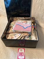 Open black metal tin showing a large stack of vintage greeting cards inside.