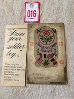 Photo of the front side of the embroidered postcard, showing floral and flag embroidery with the message 'Souvenir from France' and 'I don't forget you'.