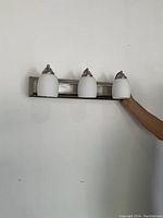 Vanity light held against a wall showing the front with three white glass shades and brushed nickel base.