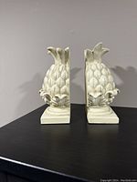 Side view of two clay pineapple bookends positioned back to back on a flat surface showing their size and design