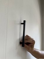 Side view photo showing the profile and depth of the black drawer pull being held by a hand, mounted on a white surface.