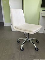 White leather desk chair positioned on a wooden floor, showing full front and side view with chrome base and wheels.