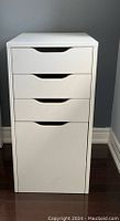 Front view of white drawer unit showing three small drawers and one large bottom drawer with curved cutout handles.