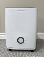 Frigidaire dehumidifier front view showing white case with circular water bucket viewing window and caster wheels.