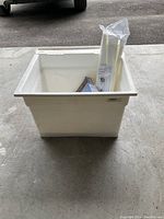 White laundry tub with accessories inside placed on concrete floor under shelter.