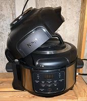 Ninja 9-in-1 Pressure Cooker Air Fryer open lid showing control panel and cooking chamber, black and stainless steel finish