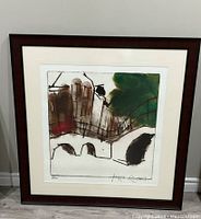 Framed square etching print featuring a stylized cityscape with green and brown tones. Artist signature visible.