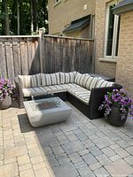 Front view of L-shaped resin wicker sectional with striped seat and back cushions on stone patio