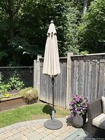 Closed patio umbrella with light beige fabric, heavy steel base, metal pole, in outdoor garden setting.