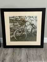 Framed photograph showing vintage bicycle against stone wall in black frame with white matting