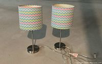 Two metal base side table lamps with colorful chevron patterned shades, clear power cords visible on concrete floor.