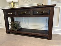 Front view of solid wood sideboard showing three drawers with brass-tone handles and open shelf
