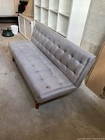 Side angle view of the medium grey tufted convertible sofa showing the overall condition, tufted back and seat, and wooden legs.