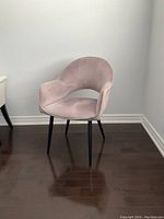 Full view of rose velvet armchair with curved back and armrests, black angular powder-coated iron legs on dark hardwood floor against white wall.