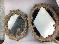 Two oval vintage mirrors together with carved solid wood acanthus leaf frames in distressed finish and visible wear.