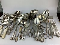 Wide view of over 60 pieces of silverplated flatware including forks, spoons, scissors, tongs, multiple patterns.