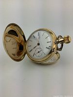 Pocket watch open at side angle showing hunter-case cover, dial and crown