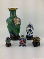 Full front view of all five cloisonné items including tall vase, snuff bottle, rectangular pill box, and two small pill boxes each on stands, against white background