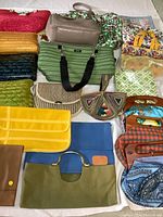 Photo showing various vintage purses and bags including woven, embroidered, fabric types, in multiple colors and styles, arranged on white surface.