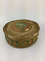 Side and top view showing the round basket with green crisscross pattern on the sides and floral lid design