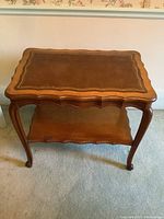 Front view of the French Provincial style coffee table showing the scalloped edges, cabriole legs, and lower shelf.