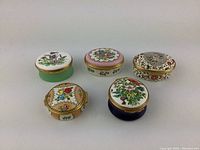 Front view of 5 enamel pill boxes showing floral designs, shapes, and colors.