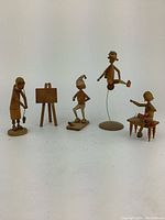 Full view of the four wood carving figures displaying various poses and objects like golf club, easel, bench, and wire-balanced figure.